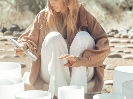 A person in a wide-brimmed hat and casual attire is sitting outdoors with multiple white bowls, seemingly playing or arranging them.