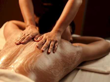 A person is receiving a back massage with their upper body covered in lotion or oil while lying face down on a massage table.