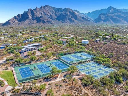 An aerial view of several outdoor tennis courts nestled in a desert landscape, surrounded by scattered houses and mountains in the background, ending the sentence.