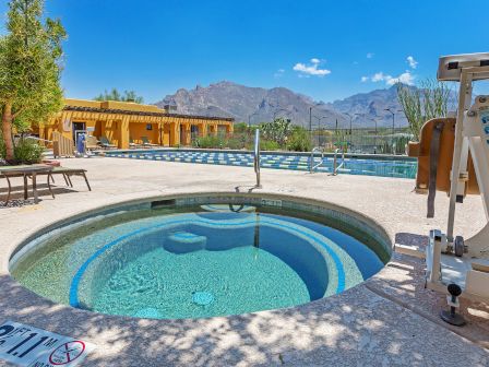 The image shows a swimming pool area with a hot tub, lounge chairs, and a mountain view in the background. There is exercise equipment nearby.