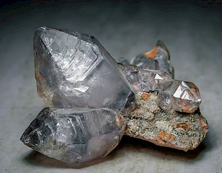 The image shows a cluster of clear, hexagonal quartz crystals attached to a piece of rock, showcasing their natural structure and transparency.