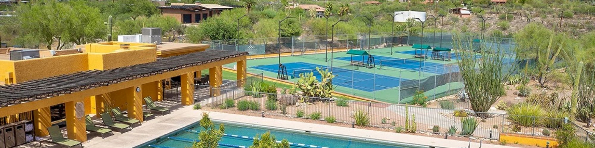 The image shows a recreational facility with a swimming pool, tennis courts, and a scenic mountain backdrop.