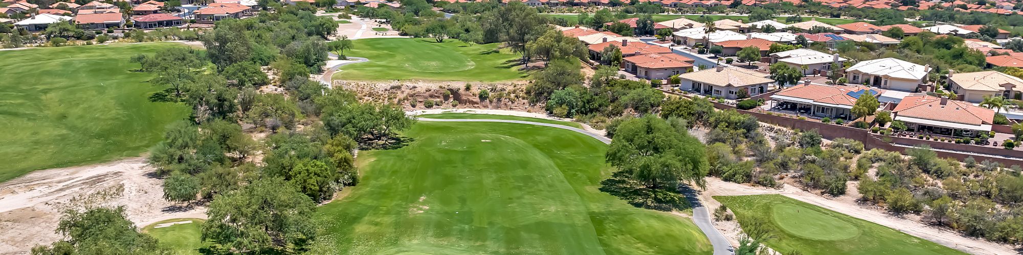 This image shows a golf course with green fairways, a residential area with numerous houses, and mountains in the background under a clear sky.