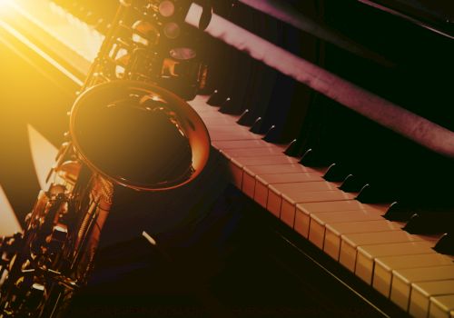 A saxophone leaning against a piano keyboard, lit by warm sunlight.