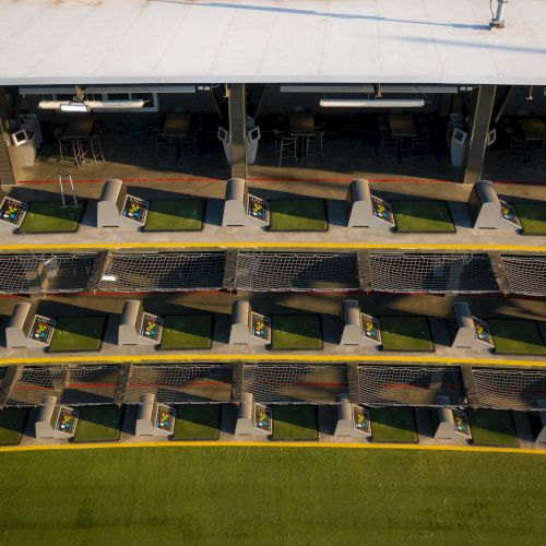 The image shows a multi-level golf driving range with several practice bays lined up in rows.