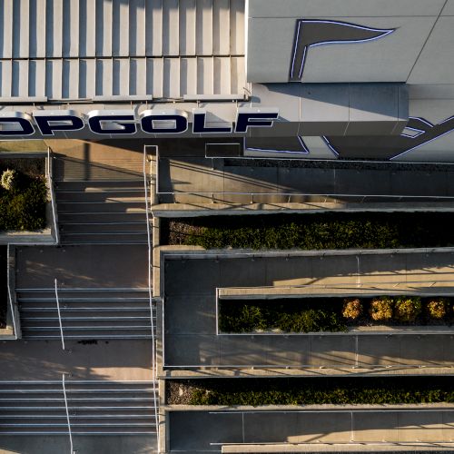 An aerial view of a building with the "TOPGOLF" sign and multiple ramps and stairs surrounded by greenery.