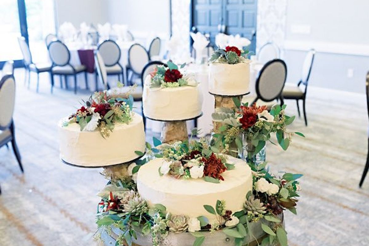The image shows a multi-tiered wedding cake adorned with floral decorations placed on a rustic wooden barrel in an elegant reception venue.
