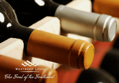 The image shows several bottles of wine stored horizontally in a wooden rack, with a logo that reads 