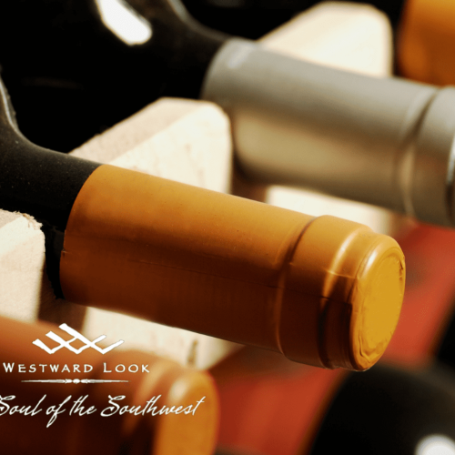 The image shows several bottles of wine stored horizontally in a wooden rack, with a logo that reads 