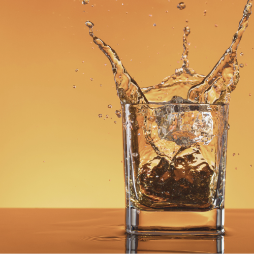 A glass with a beverage and ice cubes is in mid-splash against an orange background.