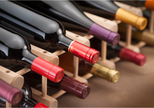 The image shows bottles of wine on a wooden rack, stored horizontally.