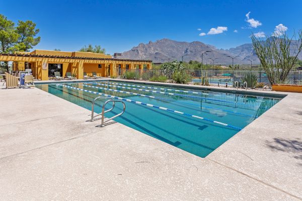 An outdoor swimming pool with lane markers, surrounded by desert landscape and mountains in the background, under a clear blue sky.