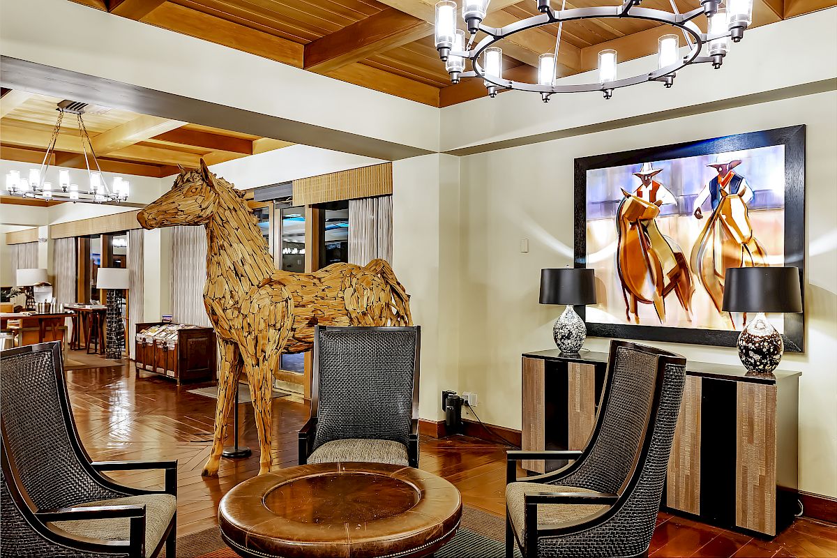 The image shows a stylish living room with wooden furniture, a horse sculpture, a round table, and a painting of horses on the wall.