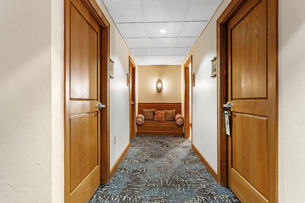 A hallway with two wooden doors on either side and a cushioned bench at the end under a wall light fixture.