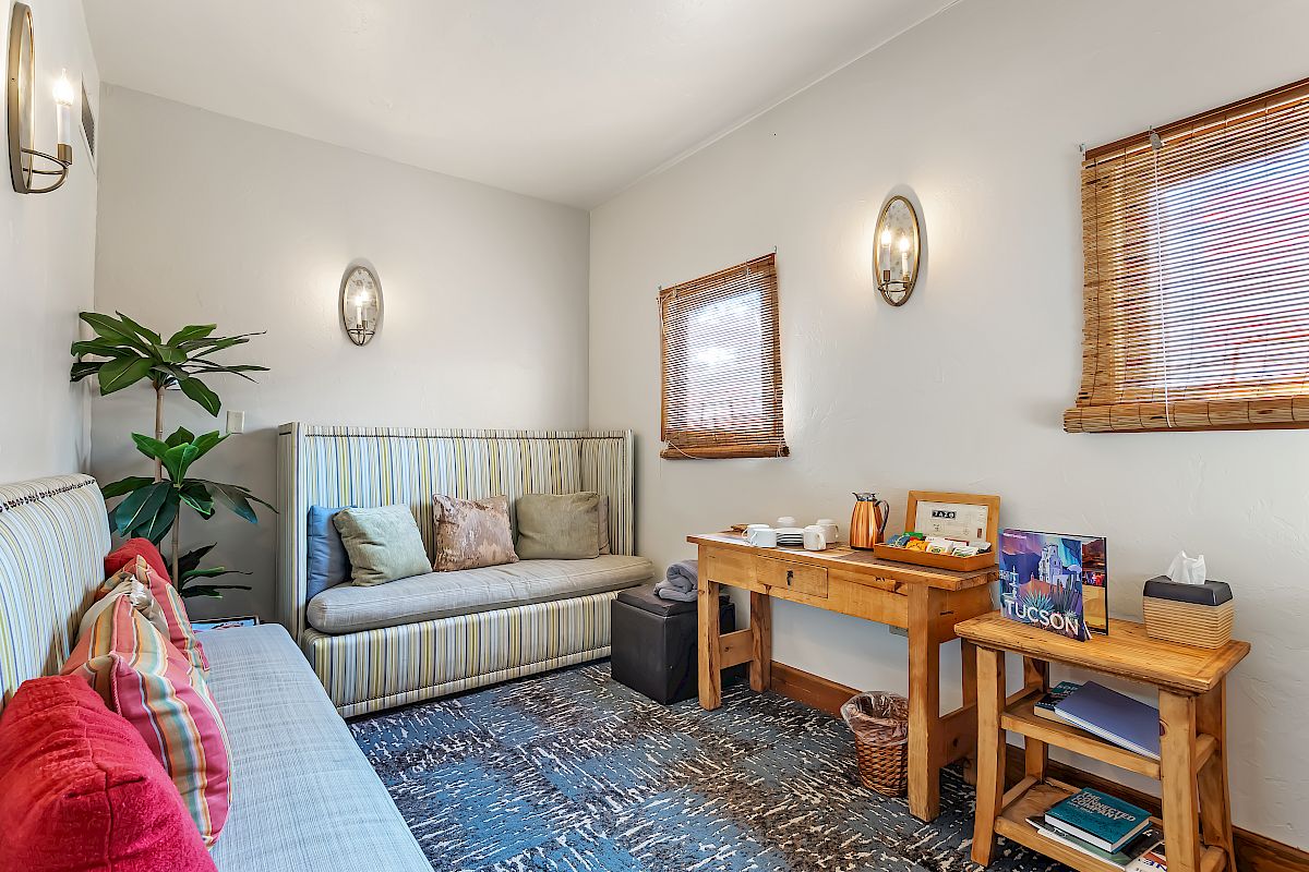 A cozy room with two sofas, a wooden desk, a plant, wall sconces, and a window with blinds; decor items are placed on the desk.