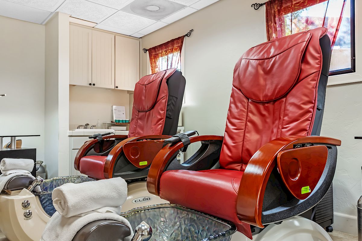 The image shows two red leather pedicure chairs with foot spas, towels, and a cabinet in the background.