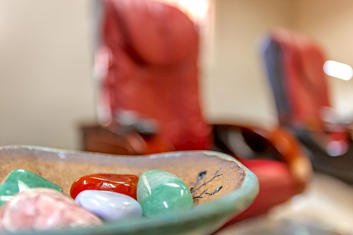 A bowl contains various colorful stones in the foreground, with blurred chairs in the background, indicating a cozy environment.