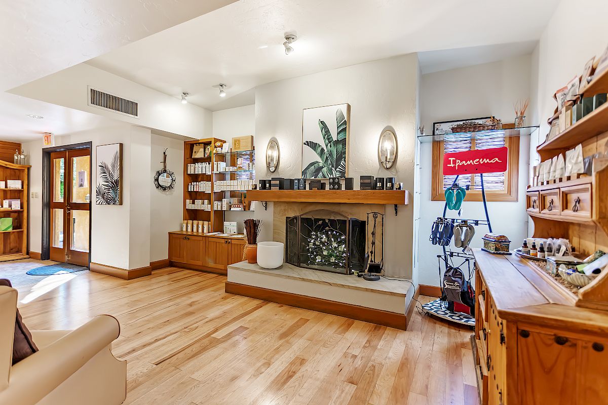 A cozy room with wooden shelves, a fireplace, a red sign, and framed art. It appears bright with natural light from a window and a glass door.