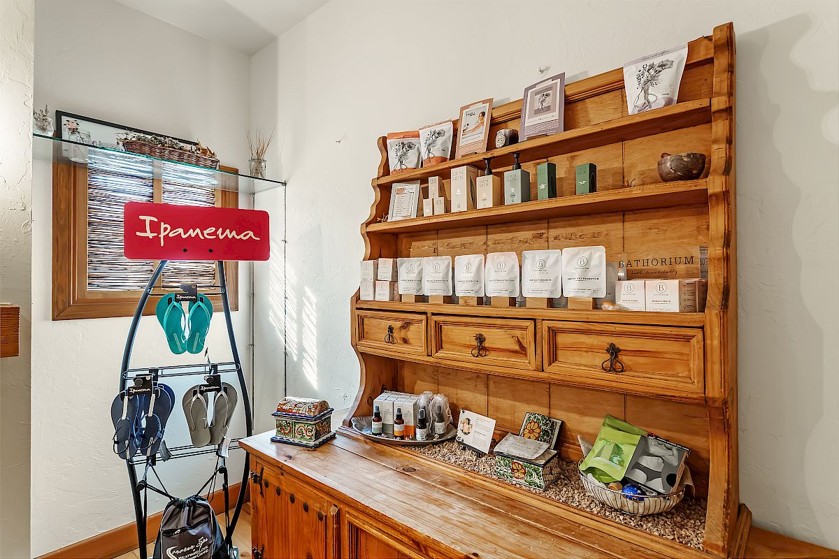The image shows a wooden shelf filled with various products and a stand with sandals and an "Ipanema" sign, in a cozy, well-lit room.