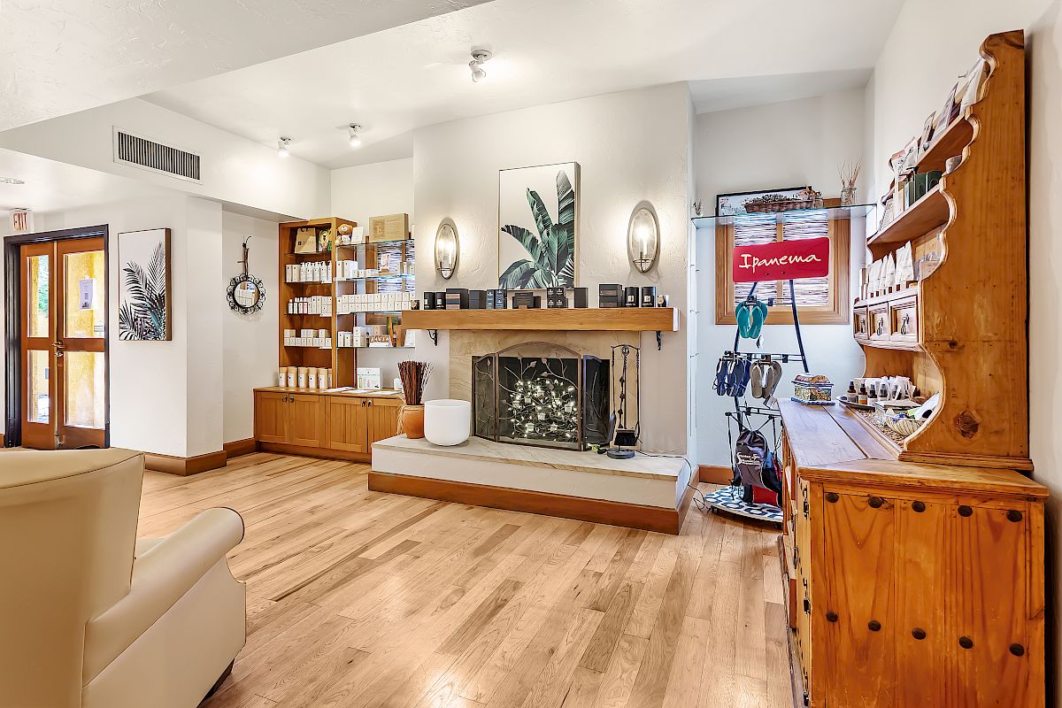 A cozy room with wooden flooring, a fireplace, bookshelves, a cabinet displaying items, and a comfy chair, well-lit with modern decor.