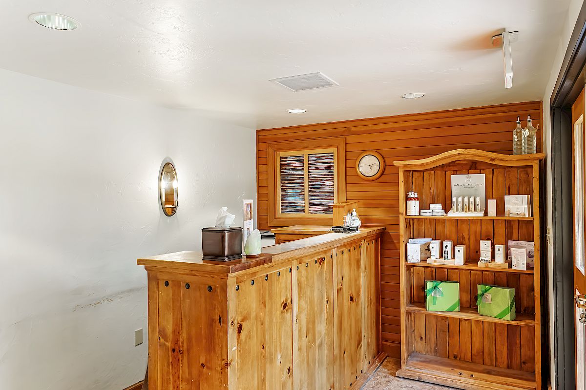 A wooden reception desk with skincare products on a shelf, a clock, and wall decor in what appears to be a spa or wellness center.