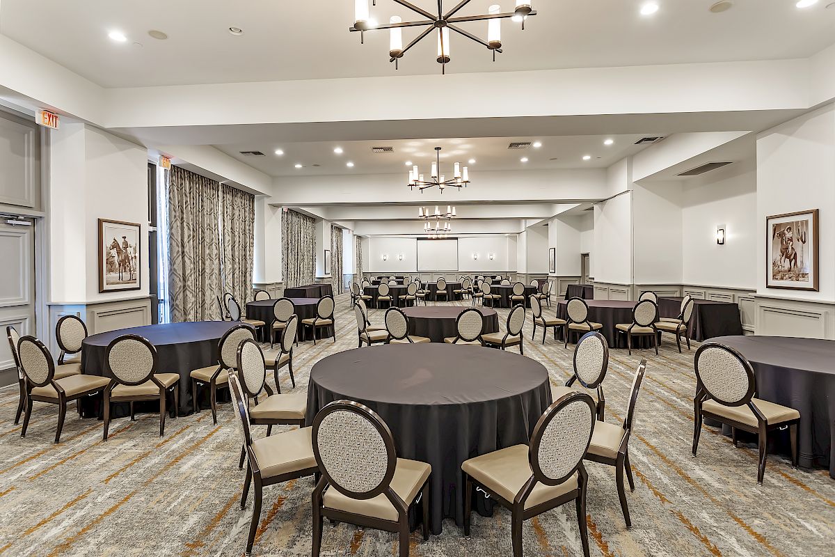 The image shows a conference room set up with round tables, each covered in a black tablecloth and surrounded by chairs.