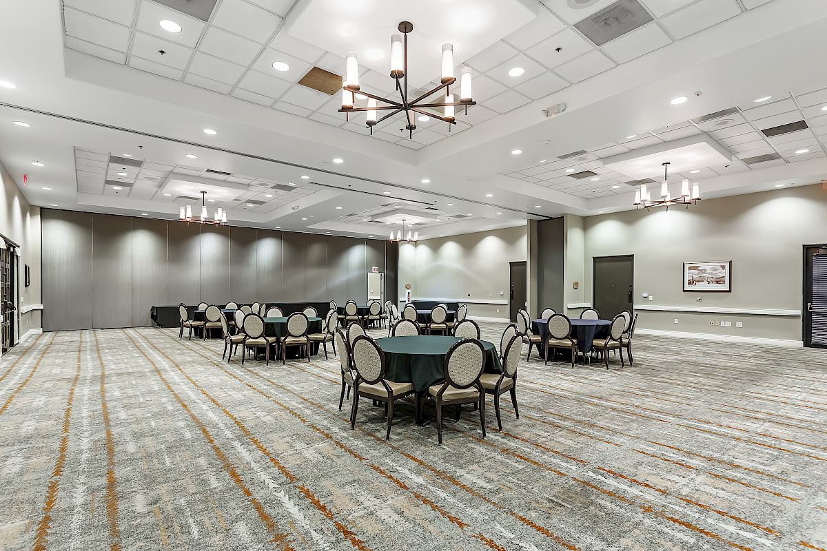 A large, modern conference room with round tables and chairs arranged throughout the space, ceiling lights, and neutral decor ending the sentence.