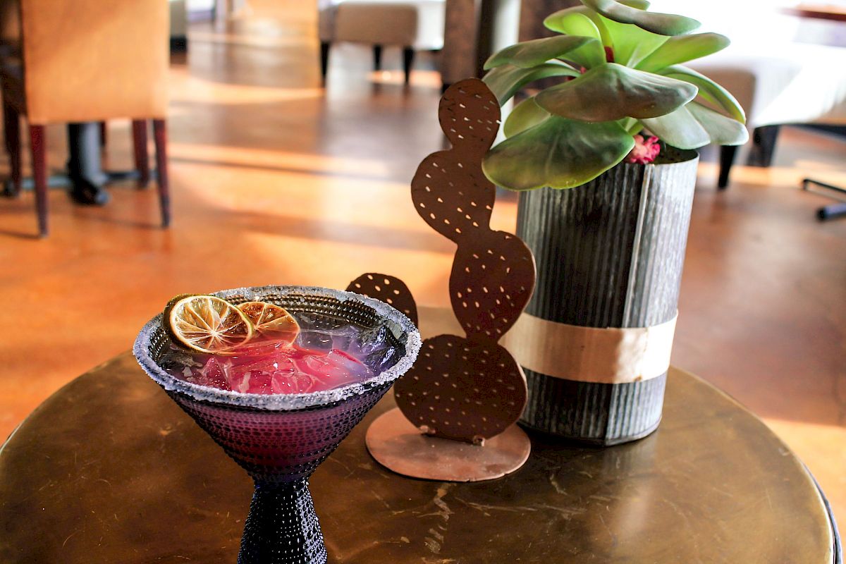 A table with a drink garnished with citrus slices, a small potted plant, and a cactus-shaped metal decoration.
