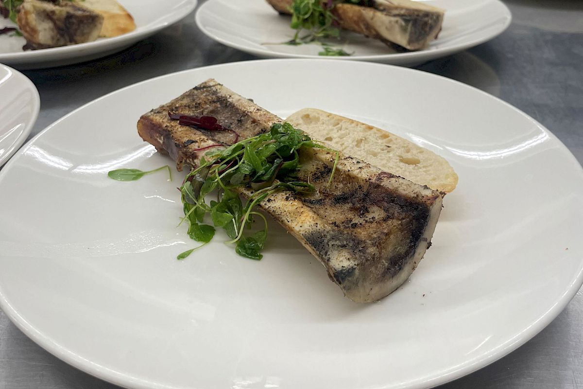 Several plates on a kitchen counter, each with a slice of bread, a piece of bone with meat, and some greens, ready to be served.