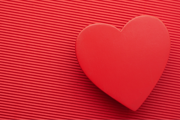 A red heart shape is resting on a textured red surface with diagonal lines, creating a simple and romantic visual.