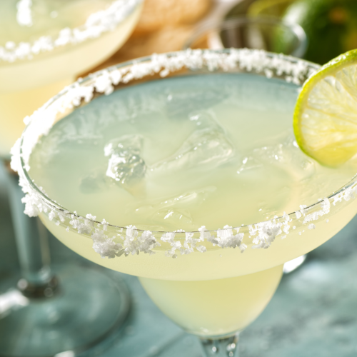 A margarita cocktail with ice and a lime garnish, served in a glass with a salted rim, is shown in the image.